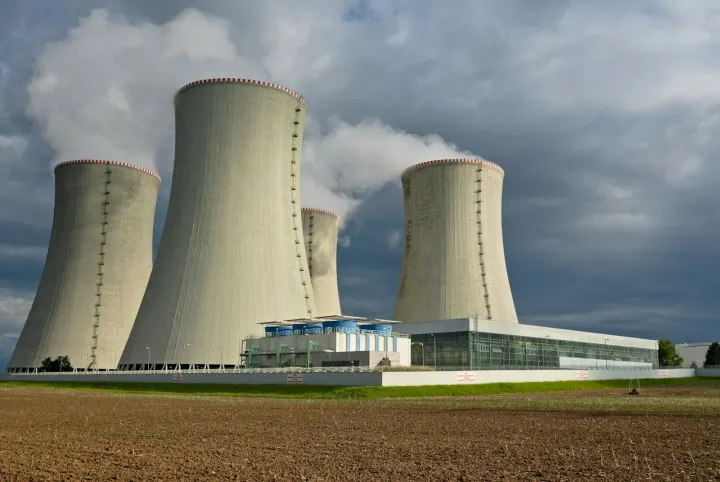 Four large concrete cooling towers emitting steam under a dark cloudy sky