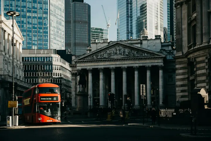 A red double decker bus driving down a street next to tall buildings